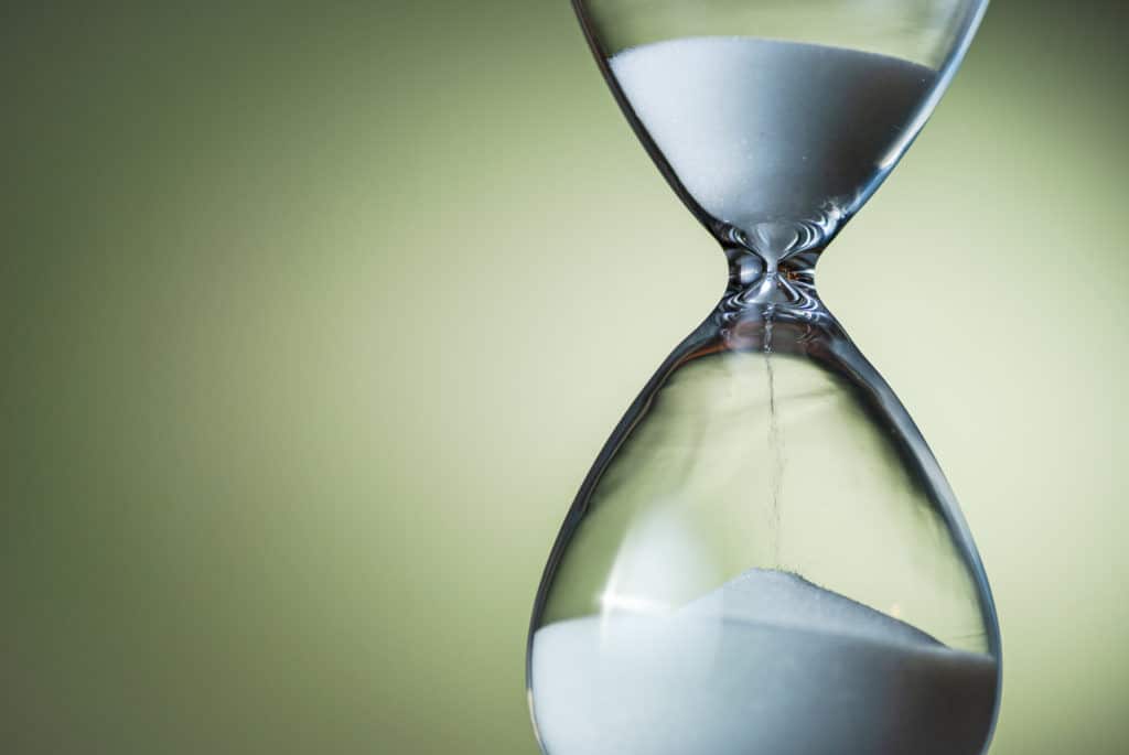 Sand running through the bulbs of an hourglass or egg timer in a concept of countdown, urgency, passing time and deadlines on green