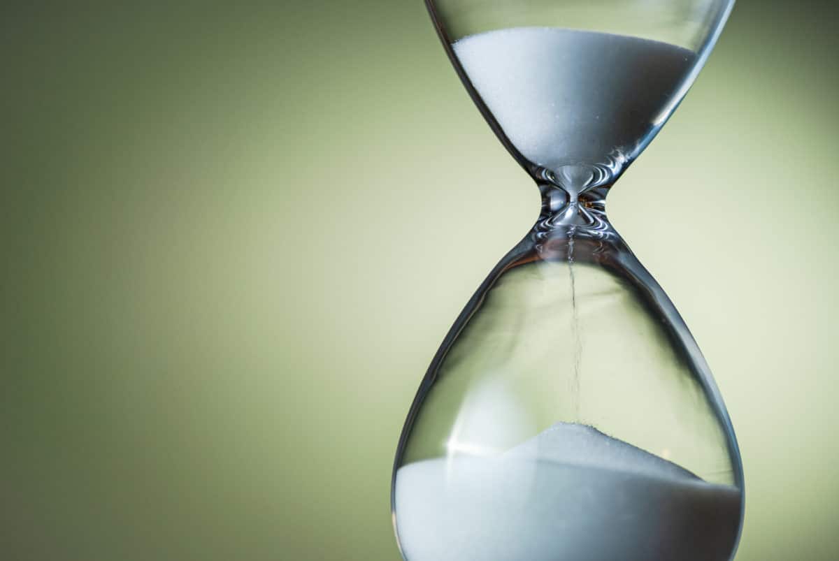 Sand running through the bulbs of an hourglass or egg timer in a concept of countdown, urgency, passing time and deadlines on green