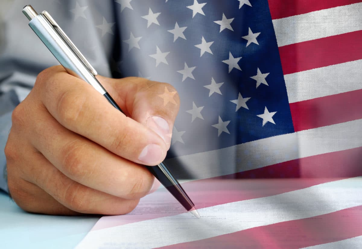 United States official signing an official document with a ballpoint pen with an overlay of the national flag the Stars and Stripes