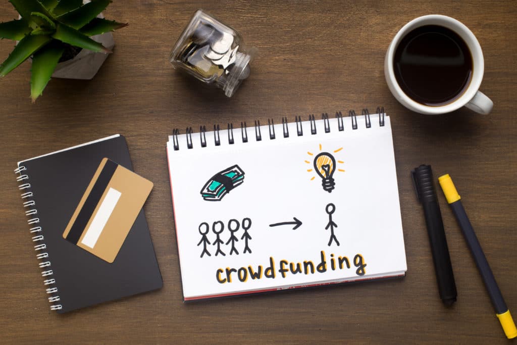 Drawing with crowdfunding concept in notepad, gold credit card and office supplies on wooden table, panorama