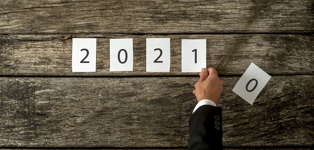 Male hand changing 2020 sign into 2021 assembled with white cards laid over a textured rustic wooden boards.